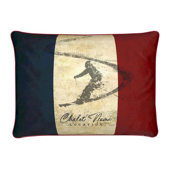 A rectangular cushion with a vintage French theme, featuring a skier silhouette and customisable text 'Chalet Name Location'. The cushion has a red, white, and blue color scheme.