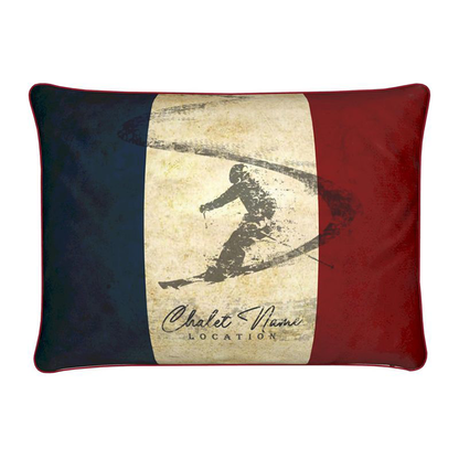 A rectangular cushion with a vintage French theme, featuring a skier silhouette and customisable text 'Chalet Name Location'. The cushion has a red, white, and blue color scheme.